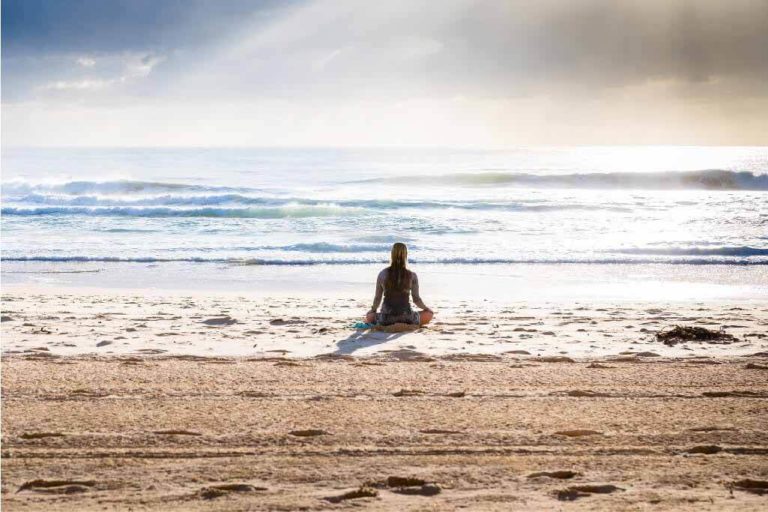 girl sitting on the beach facing the ocean in a calm setting iyengar yoga