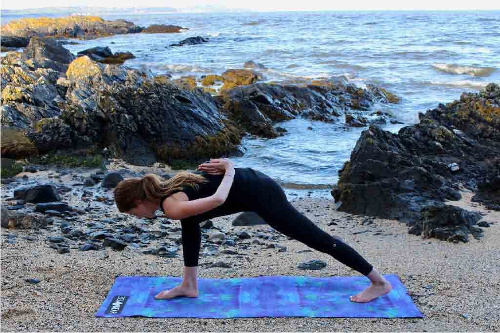 girl on yoga mat doing iyengar yoga by the ocean