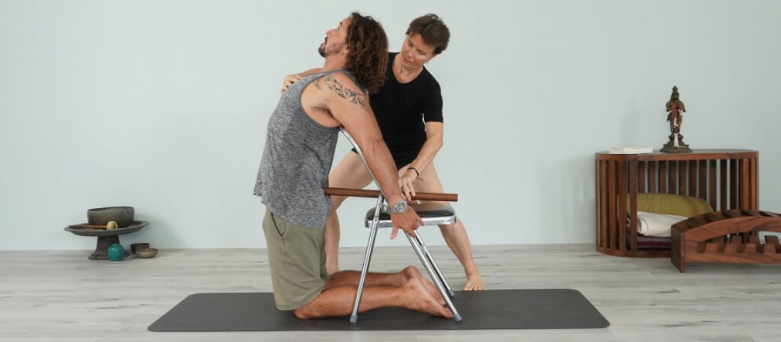 Iyengar teacher Kathy Cook helping her student get into backbend with a chair